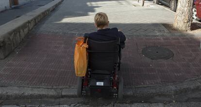 Una mujer en silla de ruedas sube un bordillo en una calle de Madrid. 