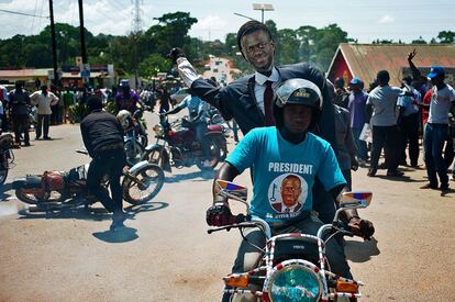 Un partidario del candidato presidencial y líder de la oposición Kizza Besigye monta en moto con una imagen de él mientras esperan su llegada en la Universidad Makerere de Kampla (Uganda). Besigye fue puesto hoy en libertad, horas después de ser arrestado por la Policía en una marcha electoral a tan solo tres días de que se celebren las elecciones presidenciales en el país.