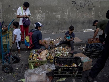 Venezolanos recogen residuos de frutas y verduras del suelo en las inmediaciones de un mercado callejero, en Caracas.