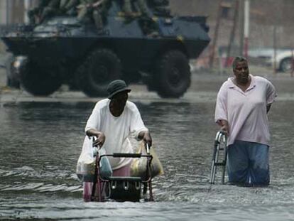 Dos personas caminan en el agua ante una patrulla de la Guardia Nacional en Nueva Orleans.