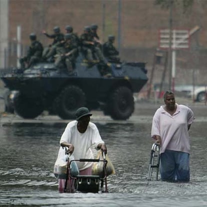 Dos personas caminan en el agua ante una patrulla de la Guardia Nacional en Nueva Orleans.