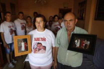 Father Toño’s parents hold up photos of their son, with the rest of the family behind them.