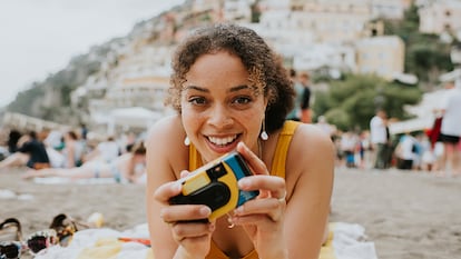 Una chica en la playa sujetando una cámara desechable