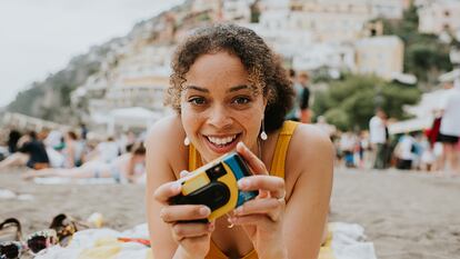 Una chica en la playa sujetando una cámara desechable