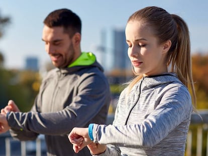 Una pareja corre por un parque y controla el ejercicio realizado con una pulsera de actividad.