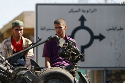 Dos rebeldes esperan en una carretera con un señal detrás donde puede leerse Trípoli, Zauiya y Subrata