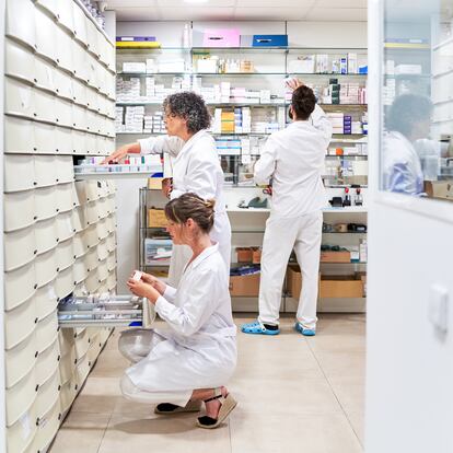 Three members of the staff looking for a medicine in a drawer of a pharmacy store