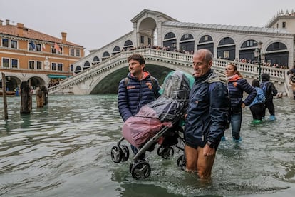 Dois turistas suspendem um carrinho de bebê para cruzar as ruas alagadas em Veneza (Itália), na segunda-feira. Ao fundo, a Ponte Rialto, que cruza o Grande Canal da cidade.