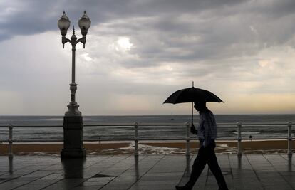 Un hombre se protege con el paraguas de la lluvia, en el paseo de muro de la playa de San Lorenzo de Gijón, el pasado 29 de agosto.