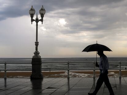Un hombre se protege con el paraguas de la lluvia, en el paseo de muro de la playa de San Lorenzo de Gijón, el pasado 29 de agosto.