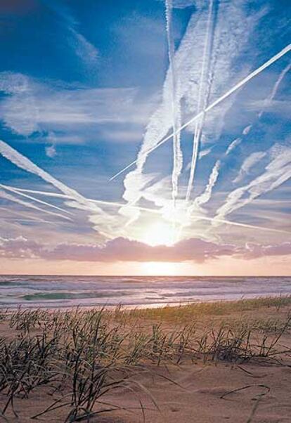 Estelas de aviones entremezcladas con nubes sobre una playa australiana.