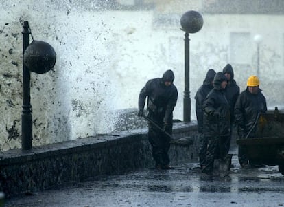 Operarios limpian los restos de fuel, procedentes del vertido contaminante del petrolero 'Prestige', en el paseo marítimo de Muxía (Coruña).