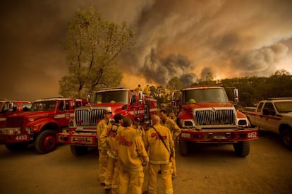 Bombeiros conversam junto a seus veículos em Clearlake com a fumaça das chamas ao fundo.