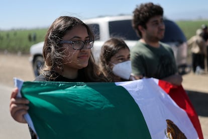 Una mujer sostiene una bandera mexicana mientras agentes federales estadounidenses bloquean la carretera Laguna Road.