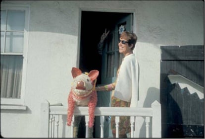 Phyllis Gebauer, amiga de Thomas Pynchon, con la piñata de cerdo y la mano del escritor asomando detrás de la puerta haciendo el signo de la paz. Fotografía tomada en California en 1965.