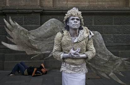 Un hombre vestido de ángel actúa en la calle mientras otro hombre yace en el suelo detrás de él en la Plaza de Armas en el centro de Santiago, en Chile.