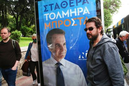 Varios peatones pasan en Atenas junto a un cartel del partido gobernante Nueva Democracia donde aparece una foto del primer ministro Kyriakos Mitsotakis, el 15 de mayo de 2023.