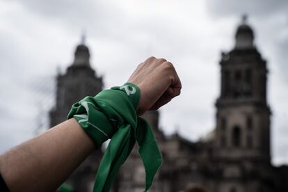 Un puño en alto con un pañuelo verde frente a la catedral metropolitana de fondo.