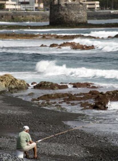 Un pescador en las playas de San Cristobal, en Las Palmas. Al fondo, los restos del Castillo, del siglo XVI.