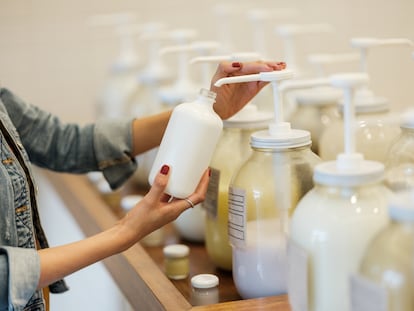 Young woman filling container with body lotion at store