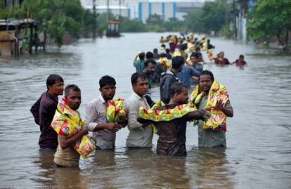 Hombres cargan paquetes de aperitivos después de recibir comida de voluntarios en un barrio inundado tras las fuertes lluvias en Ahmedabad, India.