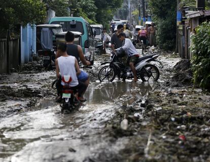 Filipinos transitan por una vía inundada y cubierta de lodo, en Noveleta, Cavite (Filipinas).