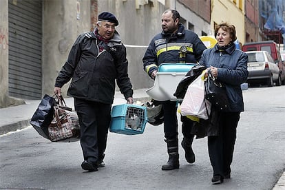 Afectats per l'enfonsament del Carmel surten de recollir estris dels seus domicilis acompanyats per un bomber.