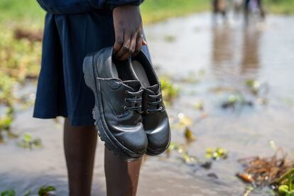 Una niña camina con los zapatos en la mano hacia la escuela de Runyu.