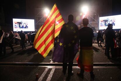 Dos jóvenes con banderas españolas, catalanas y europeas escuchan el discurso de Inés Arrimadas.