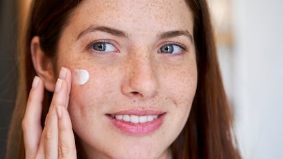 Chica joven poniéndose crema hidratante facial.