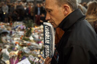 Un hombre con un ejemplar de la revista 'Charlie Hebdo' rinde homenaje a las víctimas en 'Le Carillon'.