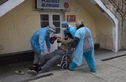 Tres sanitarios levantan a un hombre que estaba tirado en el suelo a la entrada del hospital General y lo llevan en una silla de ruedas a la sala de emergencias que trata a las personas con síntomas de covid-19 en La Paz (Bolivia).