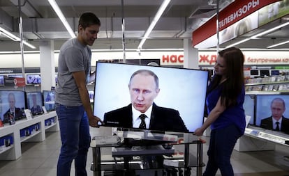 Dos empleados colocan una televisión en una tienda de electrónica en Moscú (Rusia). El presidente ruso, Vladímir Putin, volvió a cargar contra Turquía y su liderazgo, a quien acusó de 'llenarse los bolsillos con el crudo robado' en Siria e Irak, en su tradicional alocución sobre el estado de la nación.