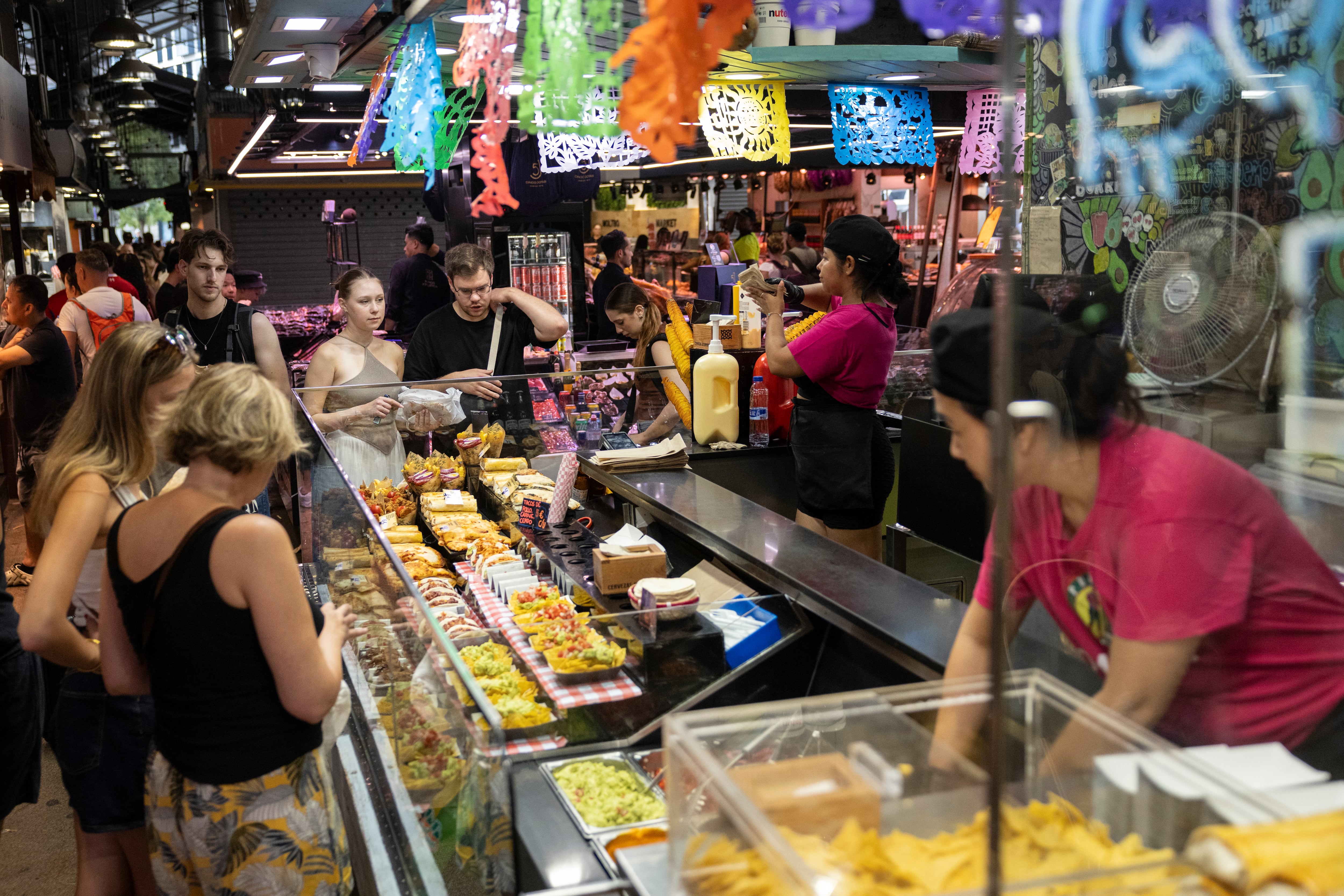 Puesto de La Boqueria de Barcelona con turistas comprando la comida en raciones para llevar que ofrecen.