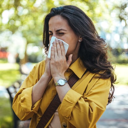 Portrait of unhealthy cute  female in yellow top with napkin blowing nose, looks to the source of the allergy, place for advertising. Rhinitis, cold, allergy concept. Pollen allergy symptoms