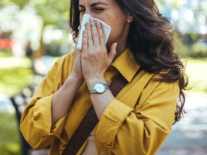 Portrait of unhealthy cute female in yellow top with napkin blowing nose, looks to the source of the allergy, place for advertising. Rhinitis, cold, allergy concept. Pollen allergy symptoms