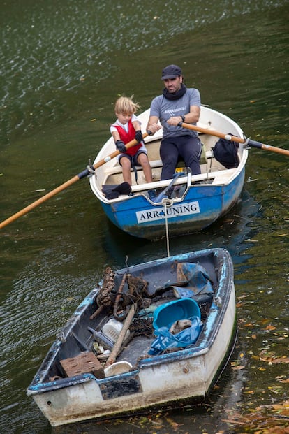 Unai Elizasu transporta con la ayuda de un niño una barcaza con residuos arrojados al río Urumea de San Sebastián.