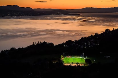 Imagem tirada do Mont de Gourze em Riez (Suíça), um campo de futebol iluminado durante o entardecer sobre o lago Lemán.