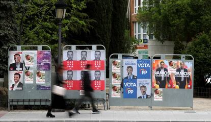 Dos personas caminan ante varios carteles electorales, durante la última campaña para las generales.