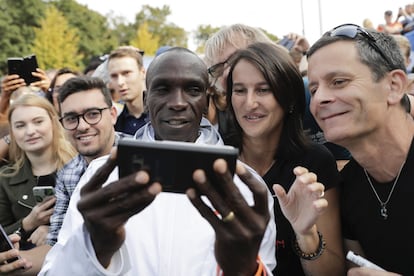 Eliud Kipchoge, ganador del maratón de Berlín, se fotografía con varios seguidores después de cruzar la línea de meta.