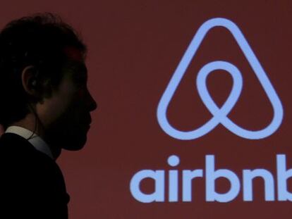 Un hombre pasea junto a un logotipo de Airbnb.