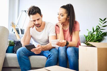 Una pareja seria sentada en el sofá en una nueva casa revisando facturas.