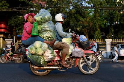 Una mujer sujeta una montaña de verduras mientras circula con una moto, en Phnom Penh (Camboya).