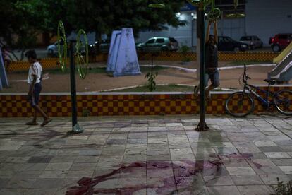 Crianças brincam diante de marca de sangue onde pouco antes ocorreu um homicídio, em Natal.