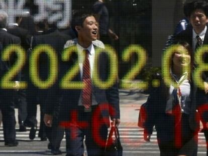 Oficinistas nipones, con su atuendo habitual, pasan por delante de una pantalla de cotizaciones en Tokio.
