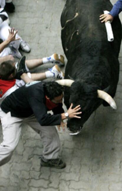 Un toro de la ganadería gaditana de Núñez del Cubillo embiste a varios mozos en la entrada al callejón de la Monumental de Pamplona, durante el tercer encierro de los <i>sanfermines</i>.