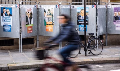 Una mujer pasea en bicicleta junto a varios carteles electorales en una calle de París, Francia.