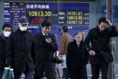 Varios hombres caminan junto a un panel electrnico que muestra el selectivo Nikkei en Tokio,  que hoy abri con una subida del 0,40 por ciento. EFE/Archivo