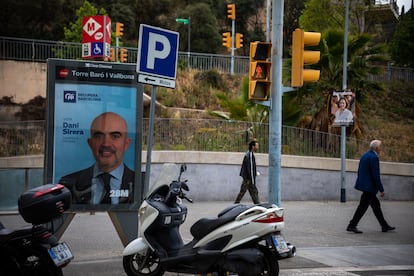 Varias perosnas pasean a la salida del metro Torre Baró Vallbona junto a carteles de candidatos a las elecciones del 28M.