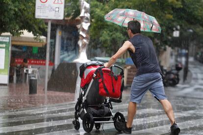 Un padre (de espaldas) empuja un carrito de bebé bajo la lluvia en Terrassa (Barcelona), en 2019.